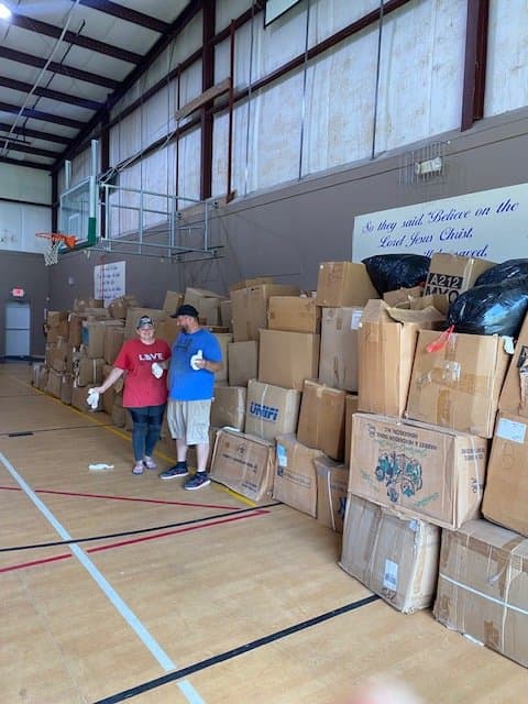 Two people standing in a gymnasium filled with stacks of cardboard boxes for a charity event.