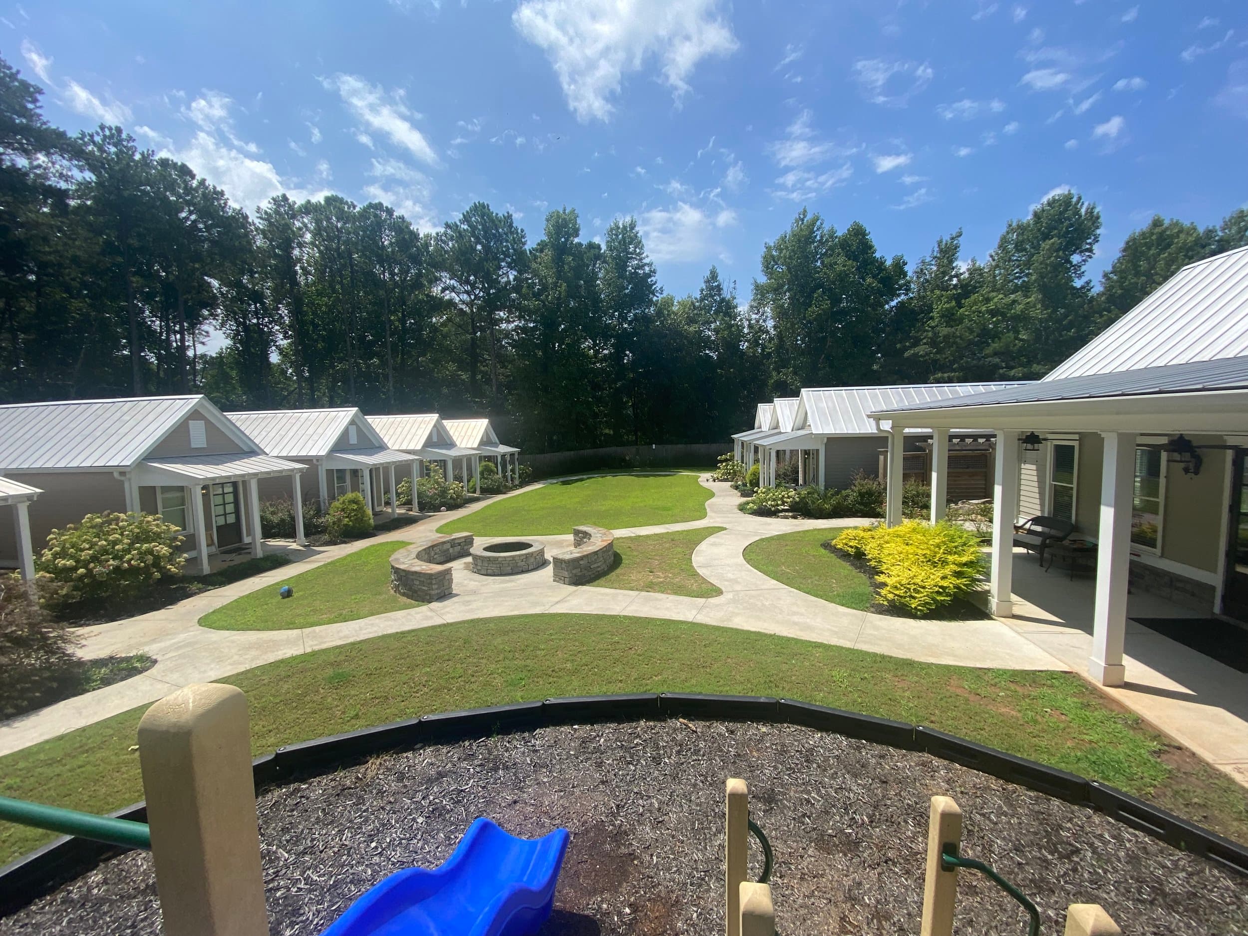 Rendering of a residential neighborhood with small houses, a grassy courtyard with a fire pit, walking paths, and a playground