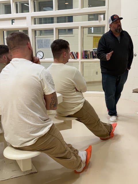 A man giving a presentation to three young men seated on a bench