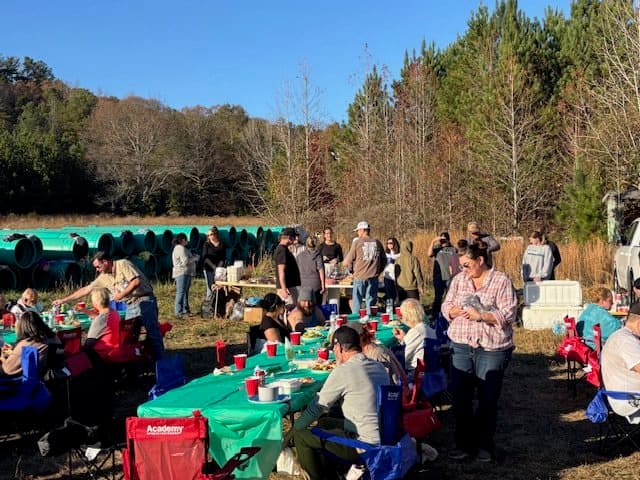 People gathered outdoors around tables with food and drinks in a natural setting